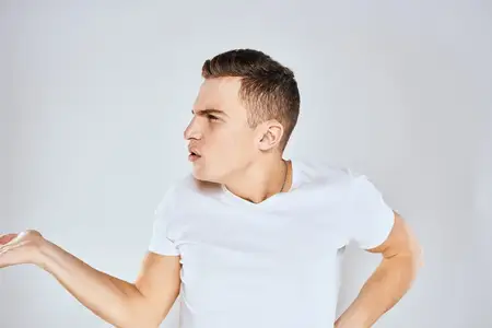 Симпатичный мужчина в белой футболке жестикулирует руками, выражая удивление, в студии