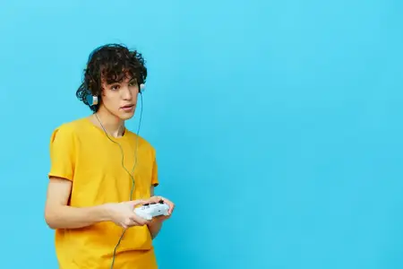 Кудрявый парень играет с джойстиком в жёлтой футболке, технологии
