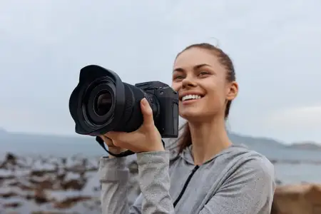 Молодая женщина запечатлевает прекрасные моменты с помощью фотоаппарата на пляже, одетая в серую толстовку