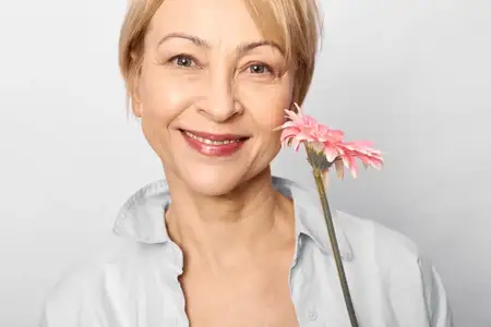 Крупный план женщины-медсестры с улыбкой, держащей розовый цветок герберы на белом фоне