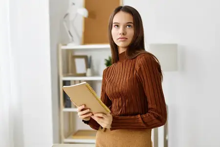 Молодая девушка-подросток европеоидной расы сидит одна за столом и читает книгу