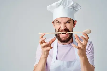 Эмоциональный повар работает на кухне, занимаясь приготовлением пищи