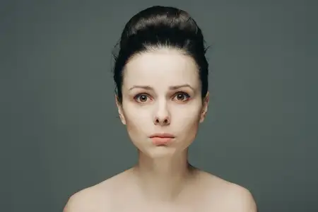 Женщина с обнажёнными плечами, чистой кожей и собранными волосами, передающая эмоции