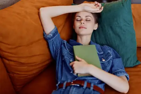 Отдыхая дома, женщина лежит на диване с книгой в руке, наслаждаясь спокойным моментом чтения