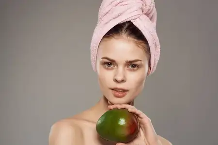 Женщина держит манго в руках, её плечи обнажены, кожа чистая