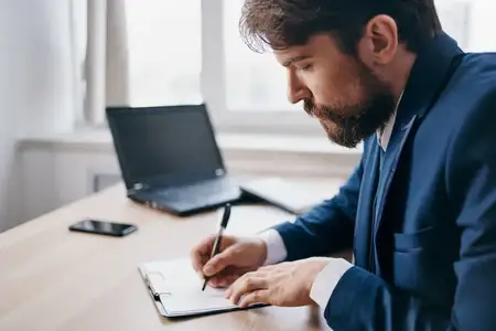 Бородатый мужчина работает за ноутбуком в офисе, на его лице читаются профессиональные эмоции