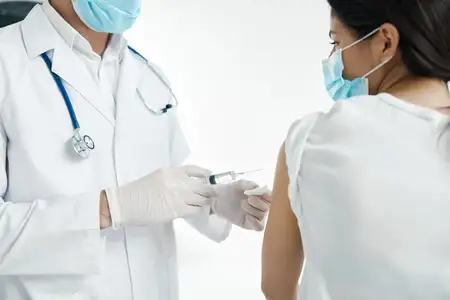 Врач со шприцем в руке делает инъекцию вакцины в защитных перчатках
