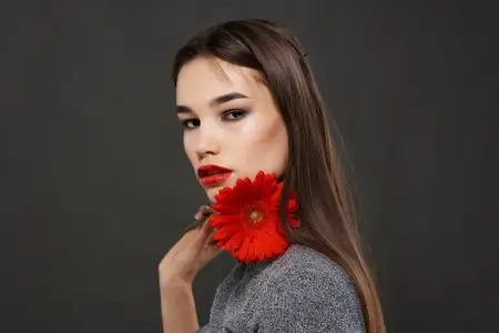 Красивая женщина с ярким макияжем и красным цветком у лица, гламур