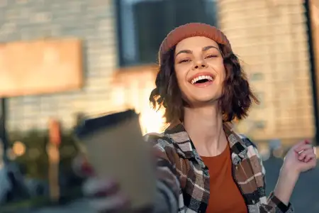 Женщина делает селфи с улыбкой в теплом золотистом свете в городской обстановке