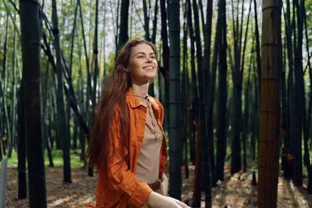 Женщина улыбается в бамбуковом лесу с длинными волосами и в оранжевой куртке