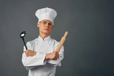 Весёлый повар в униформе держит в руках кухонные принадлежности
