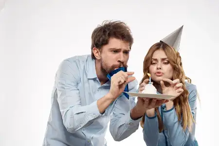 На корпоративной вечеринке мужчина и женщина веселятся рядом с праздничным тортом со свечой