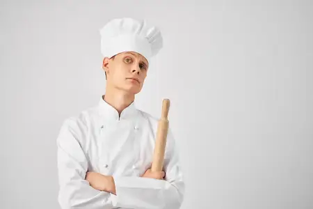 Мужчина в форме шеф-повара держит в руках колокольчик на светлом фоне