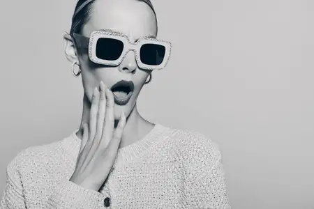 Модная белая женщина с бледной кожей с шокированным выражением лица в больших солнцезащитных очках и вязаном свитере на нейтральном фоне для концепции стиля