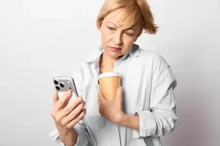 Взволнованная пожилая женщина держит смартфон и кофе