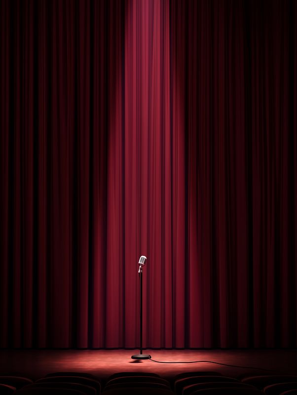 Vintage microphone stands center stage before closed red velvet curtains, bathed in a lone spotlight, evoking drama and anticipation for performance, speech, comedy, or rehearsal.