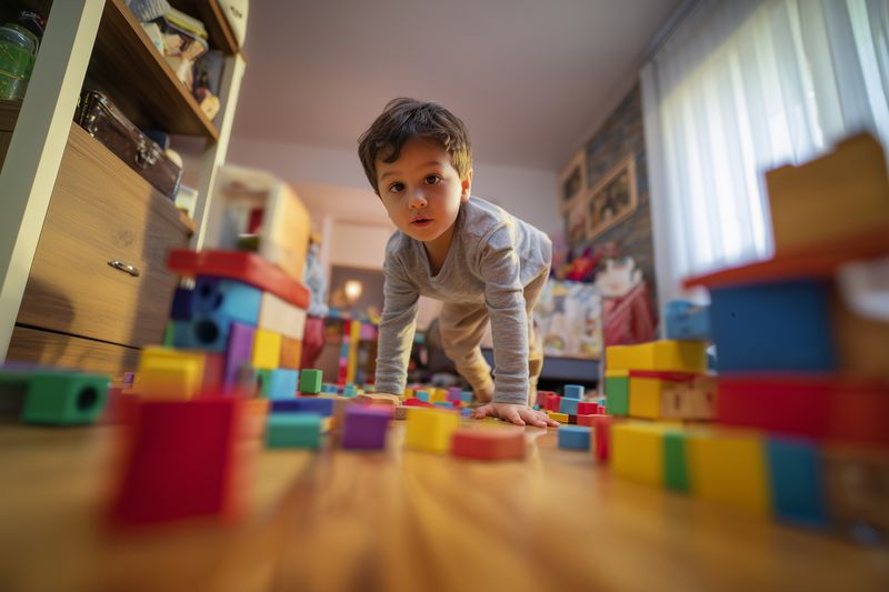 Curious toddler crawling among colorful wooden blocks scattered across a cozy playroom floor, exploring toys and discovering shapes in a warm, softly lit home environment with focus.