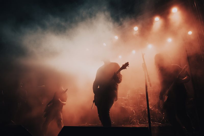 Silhouetted rock band performing on a smoky stage with dramatic backlighting and warm spotlights, creating an intense live concert atmosphere filled with movement and raw energy.