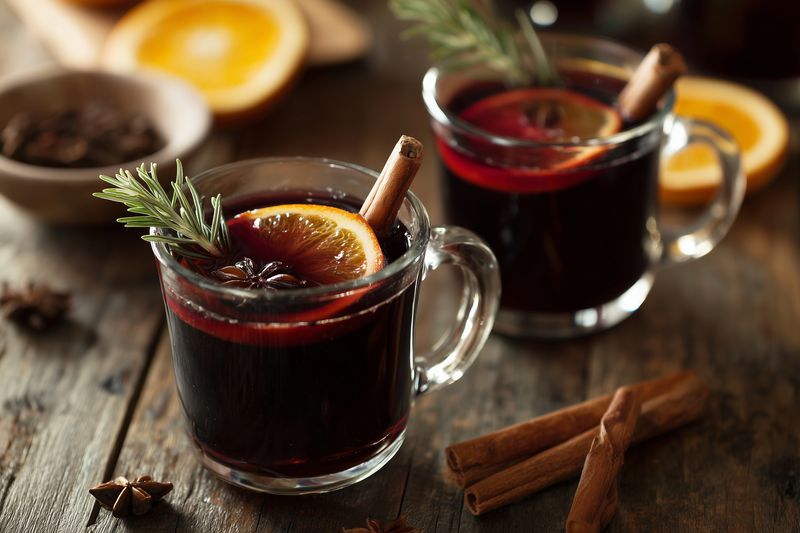 Warm spiced mulled wine in clear glass mugs with orange slices, cinnamon sticks, star anise and rosemary garnish on a rustic wooden table creating a cozy winter atmosphere
