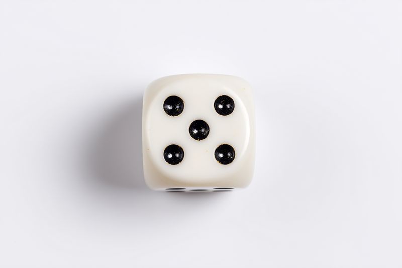 Close top view of a single white six-sided die showing five black pips on a clean white background, minimal studio composition with soft directional light, subtle shadow and glossy surface.