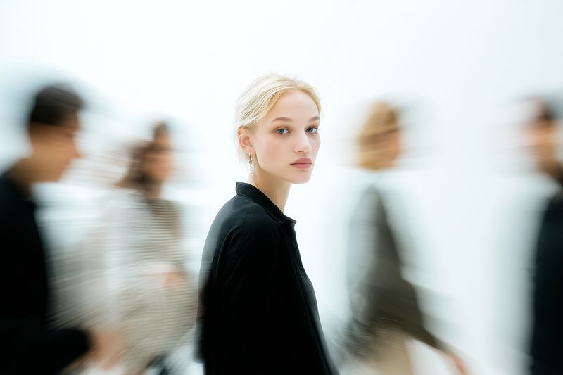 Portrait of a young woman standing calmly in focus while blurred figures rush past, conveying contrast between stillness and movement, isolation and the fast urban pace.