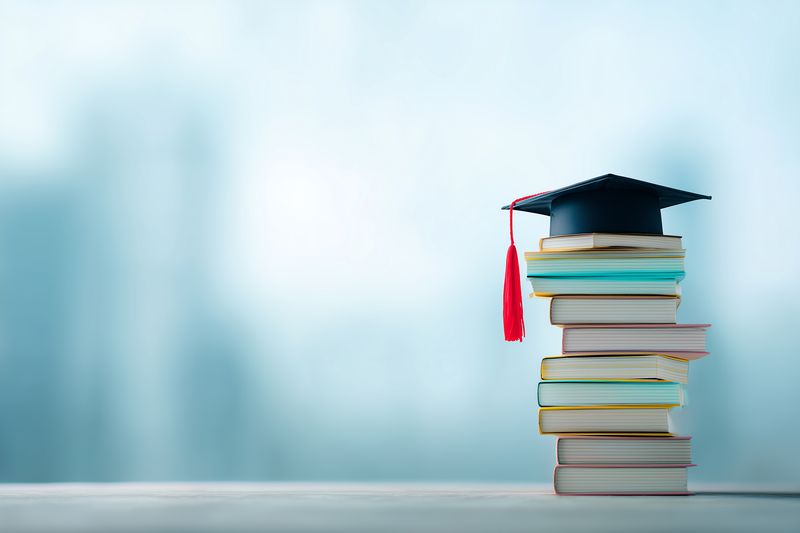 Stack of colorful books topped with a graduation cap on a soft blurred background, representing education, academic achievement, studying, knowledge, graduation, career and lifelong learning.