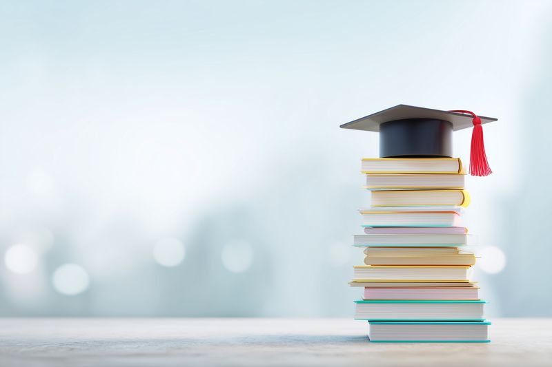 Stack of colorful books topped with a graduation cap symbolizing academic achievement, learning, study success and educational milestones with a soft bokeh background.