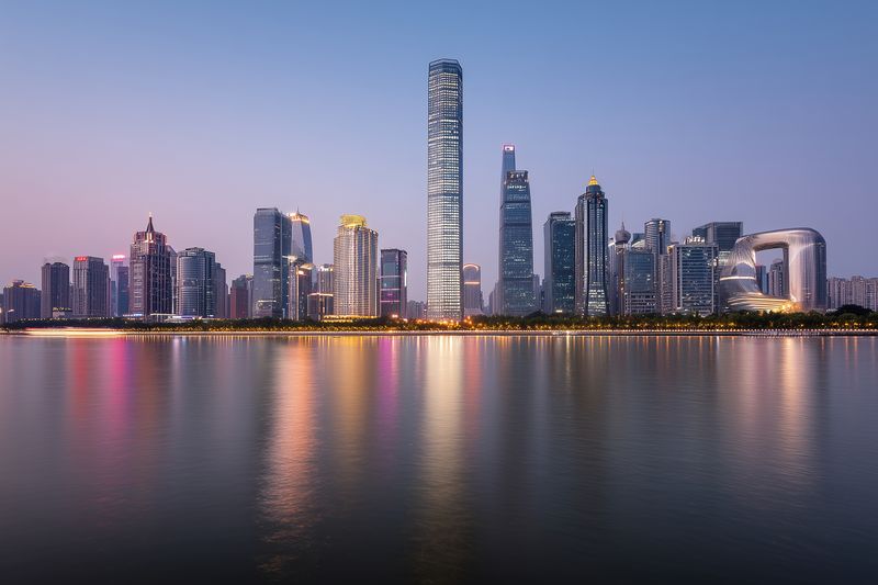 Panoramic view of a modern urban skyline with illuminated skyscrapers reflecting on calm waterfront at dusk, showcasing contemporary architecture and ambient evening lights.