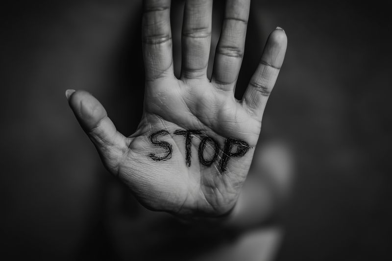Black and white closeup of an outstretched hand with the word STOP written on the palm, dramatic lighting and shallow depth of field emphasize protest, warning and refusal.
