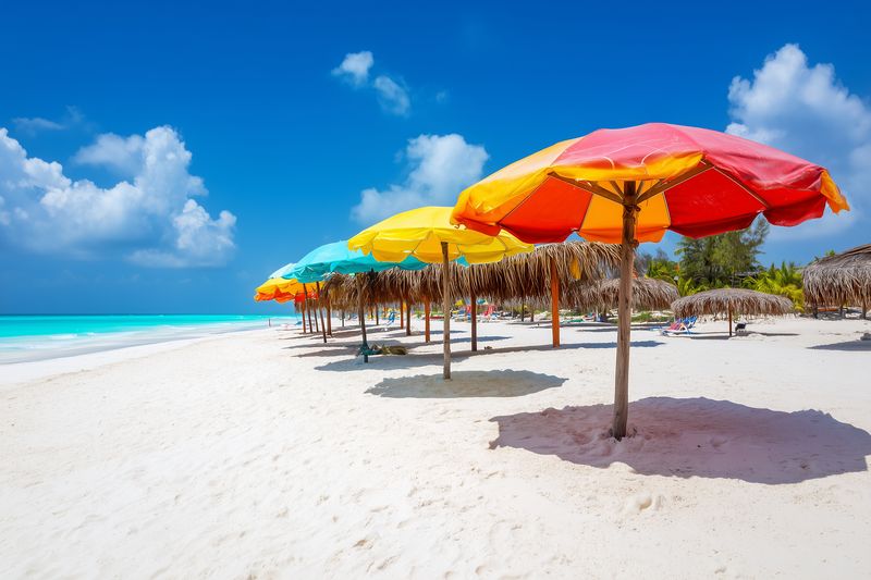 Colorful beach umbrellas line a pristine white sand shore under a bright blue sky with turquoise sea, creating a vibrant tropical scene perfect for relaxation and leisure.