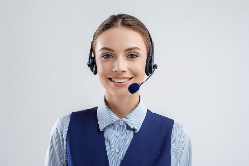 Portrait of a professional customer service representative wearing a headset and uniform vest, smiling confidently against a plain background to convey friendly support.