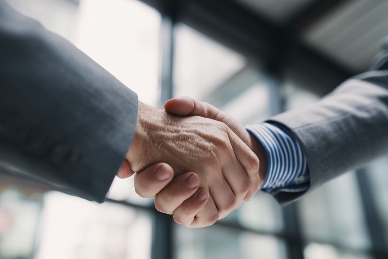 Close-up of two business professionals shaking hands in a modern office environment, symbolizing agreement, partnership and trust during a corporate meeting or successful negotiation.