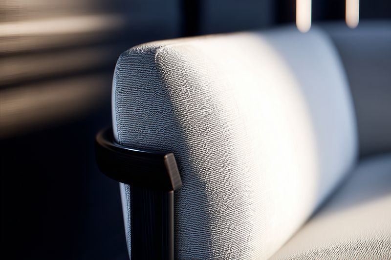 Close-up of a modern upholstered sofa armrest in soft natural light, highlighting textured fabric, visible stitching and subtle shadows to emphasize minimalist furniture design and cozy atmosphere.