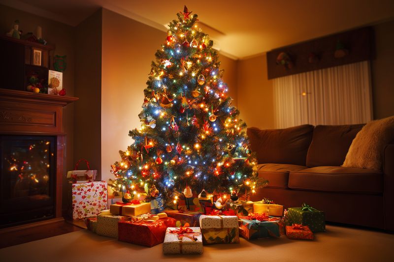 Cozy living room scene with a decorated Christmas tree glowing with multicolored lights and surrounded by wrapped presents, creating a warm festive holiday atmosphere.