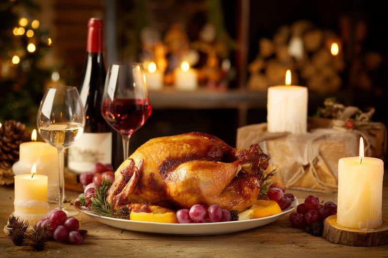 Golden roasted turkey on a festive table with candles, wine glasses and grapes, creating a warm cozy atmosphere for a holiday dinner and intimate family celebration.
