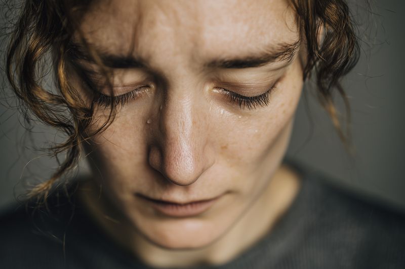 Close-up portrait of a woman with closed eyes and a single tear, conveying deep emotion and vulnerability in a soft, intimate light for editorial and conceptual storytelling use.