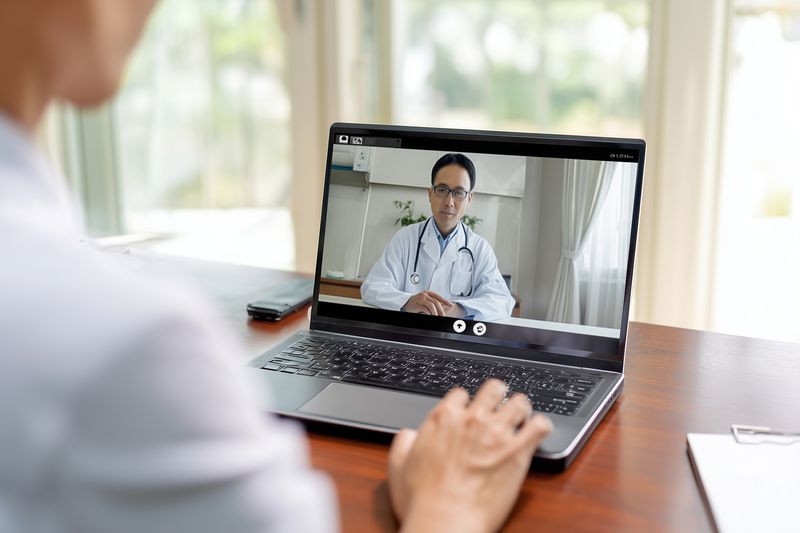 Patient using a laptop for a virtual medical consultation with a doctor visible on screen, telemedicine appointment in a home setting focusing on remote healthcare communication and convenience.