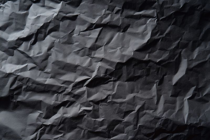 High-contrast crumpled black paper texture featuring deep folds and dramatic shadows, ideal as a moody background for design, packaging mockups, websites, and creative texture overlays.