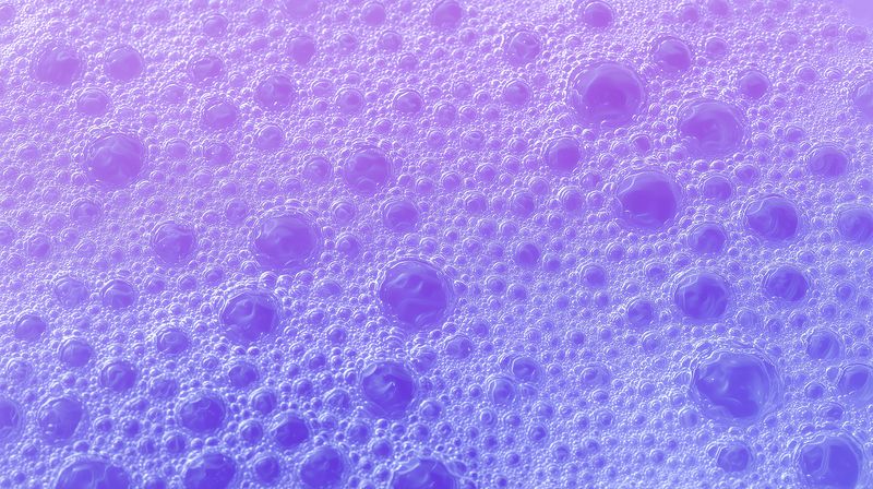 Close-up view of purple foam bubbles forming a textured abstract surface with iridescent glow and glossy spherical suds, creating a colorful pastel gradient background for creative design.