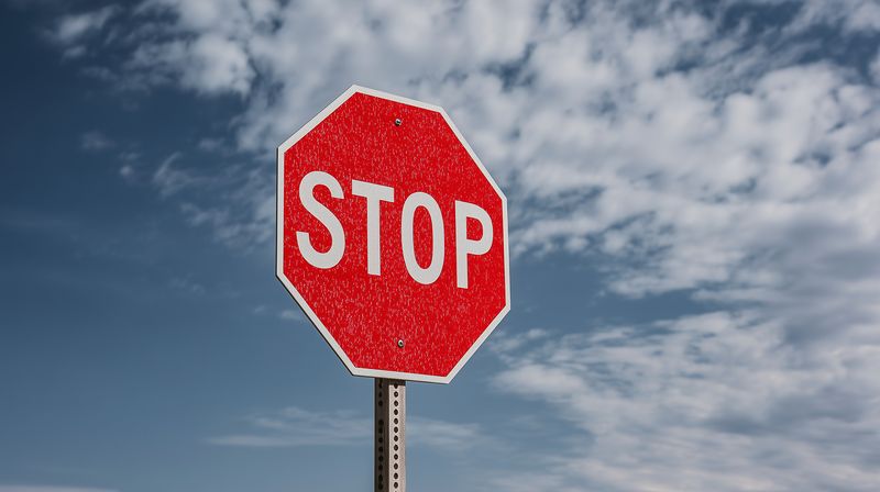 Close-up of a red octagonal stop sign covered in frost against a cloudy blue sky, symbolizing traffic safety and winter road caution for drivers and pedestrians alike.