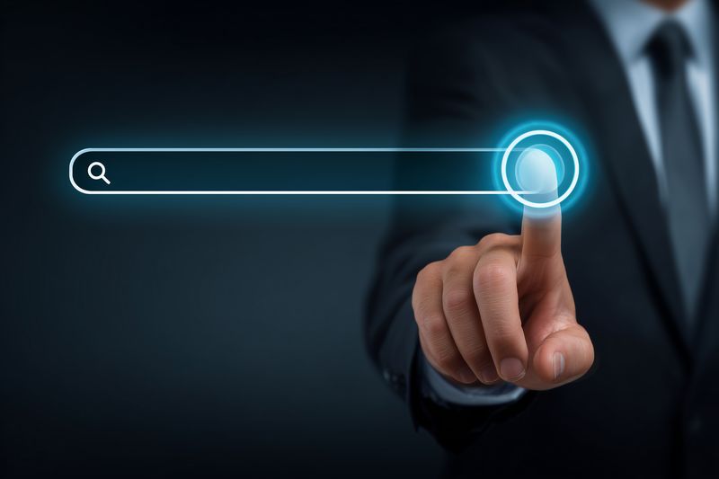 Businessman in suit touching a glowing virtual search bar on a dark background, symbolizing online search, digital interface and futuristic touchscreen technology for business research.