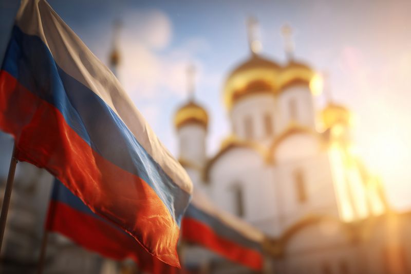 Waving tricolor flags in the foreground with sunlight illuminating a historic cathedral featuring golden domes and ornate towers, creating a warm patriotic urban scene.
