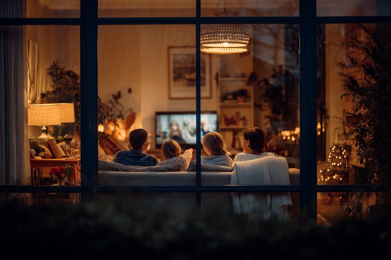 Family livingroom evening television cozy couch together lamp light relaxed holiday atmosphere with blankets adults watching movie and enjoying home comfort