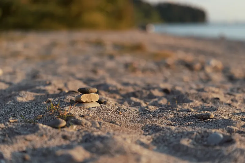 Stacked stones Zen balance on a sandy beach during sunset, creating a peaceful meditation concept with warm golden hour light along the calm blurred ocean shoreline.