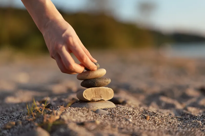Woman stack stones on sandy beach during sunset, lifestyle concept of balance, zen, calm, harmony, meditation, and peace. Close up shot of hand placing sea rocks.