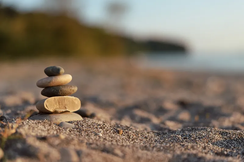 Stack of smooth stones balanced on a sandy beach during sunset. Zen meditation concept for harmony, lifestyle, and relaxation, captured with a soft blur in a peaceful outdoor nature setting.