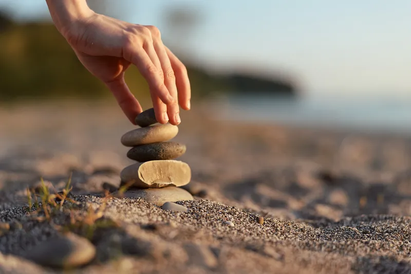 Woman stack zen stones on sandy beach lifestyle. Hand balancing river pebbles outdoors. Concept of peace, mindfulness, meditation, harmony, and meditation at sunset.