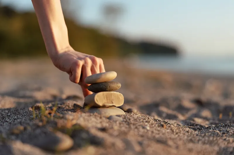 A woman lifestyle concept capturing a hand stacking stones on the beach at sunset. The balance of rocks reflects harmony and mindfulness in a peaceful outdoor nature setting.