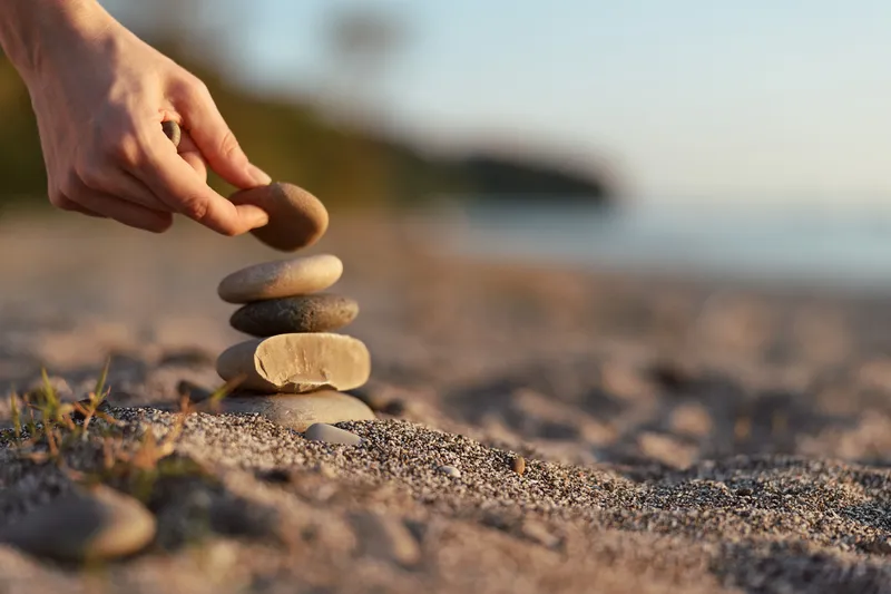 A woman lifestyle hand building a zen stone stack on a beach by the sunset sea. Concept of meditation, balance, harmony, peace, relaxation, wellness, and mindfulness.