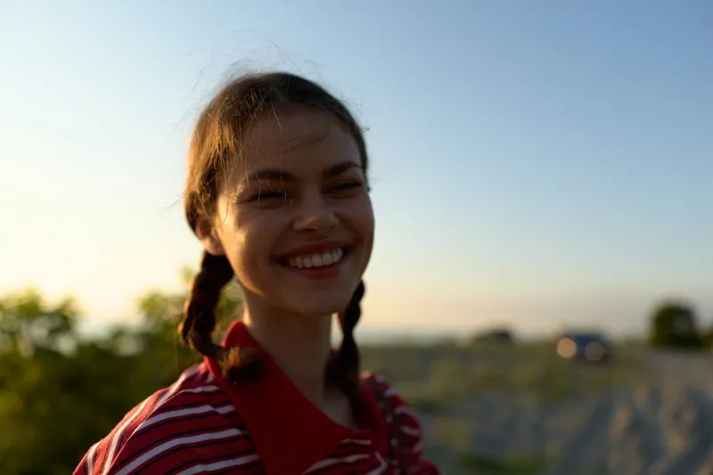A happy young woman with braids smiles as she enjoys a sunset lifestyle outdoors. The natural light creates a warm glow on her face. Concept for youth, joy and daily freedom.